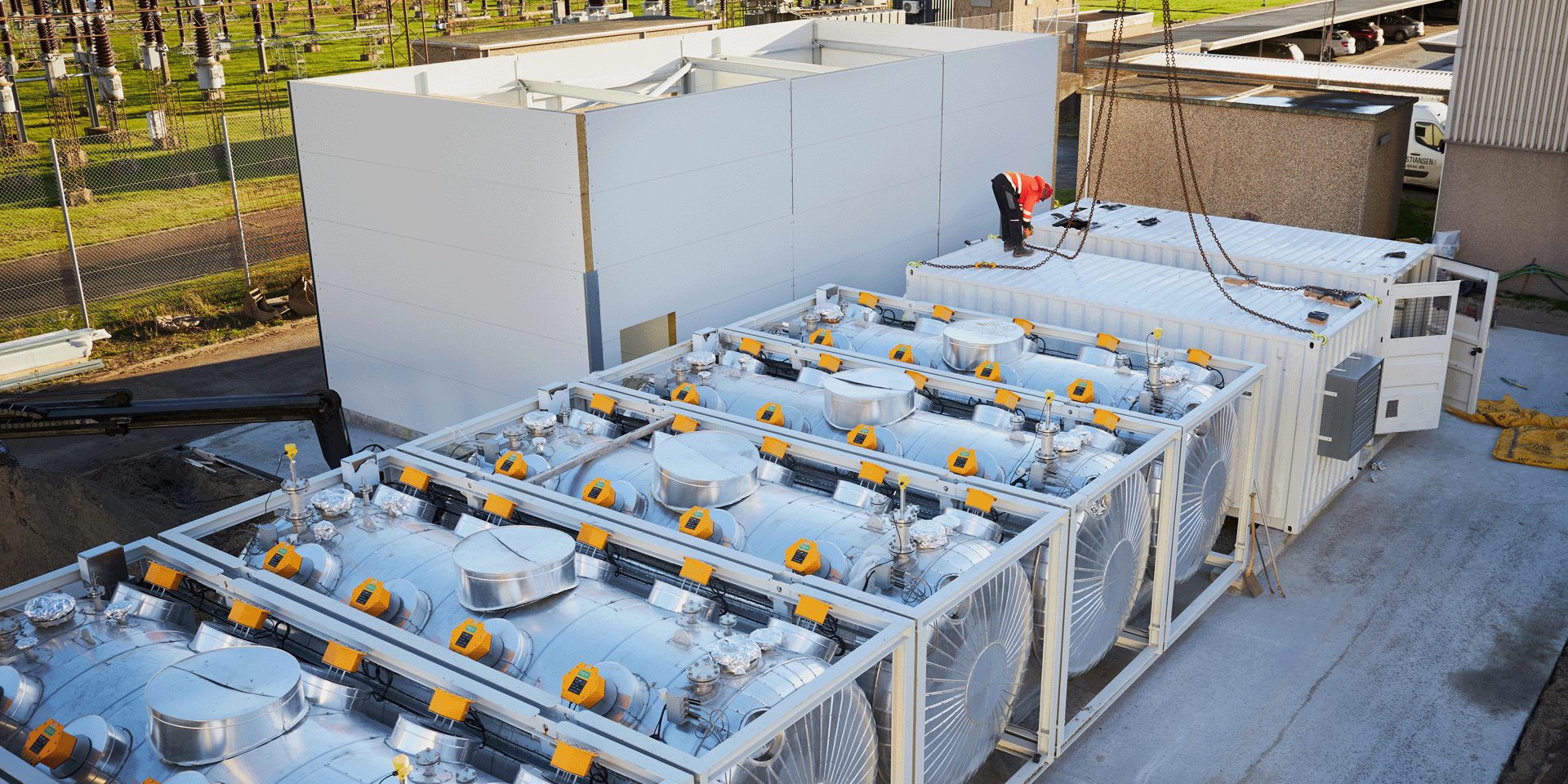 Kyoto Heatcube thermal battery on site, a worker in an orange reflex jacket stands on a white container outside.